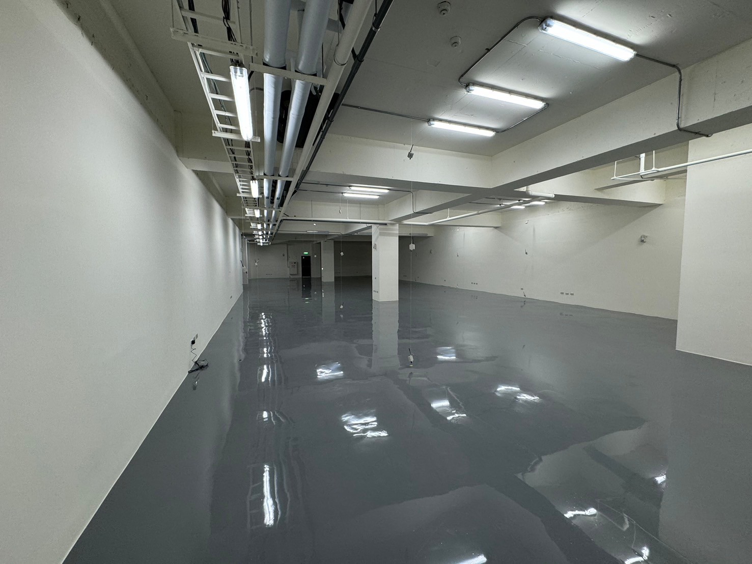 Empty white industrial room with a glossy floor and exposed ceiling pipes and fluorescent lights